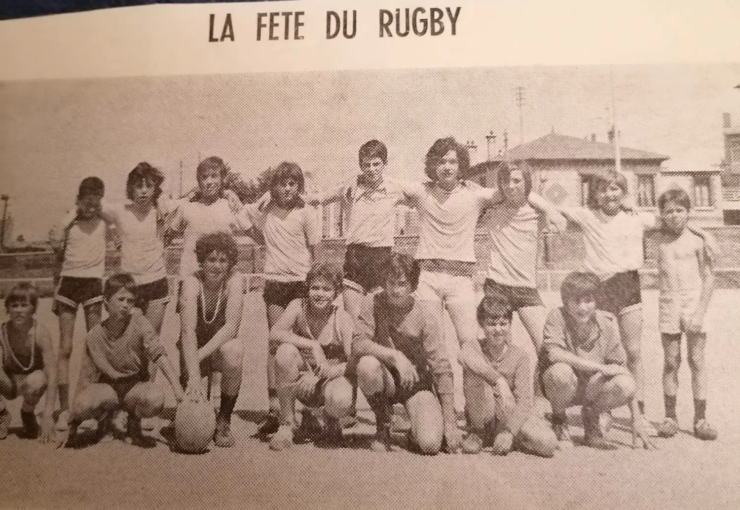 Une photo en noir et blanc montrant un groupe de jeunes garçons posant pour une photo d'équipe sur un terrain de rugby. Ils sont debout et accroupis, souriants et les bras sur les épaules les uns des autres. La plupart des garçons portent des shorts et des t-shirts. En haut de la photo, il est écrit "LA FETE DU RUGBY". Cette image fait partie de l'Histoire du Rugby Club Val de Bièvre (RCVB).